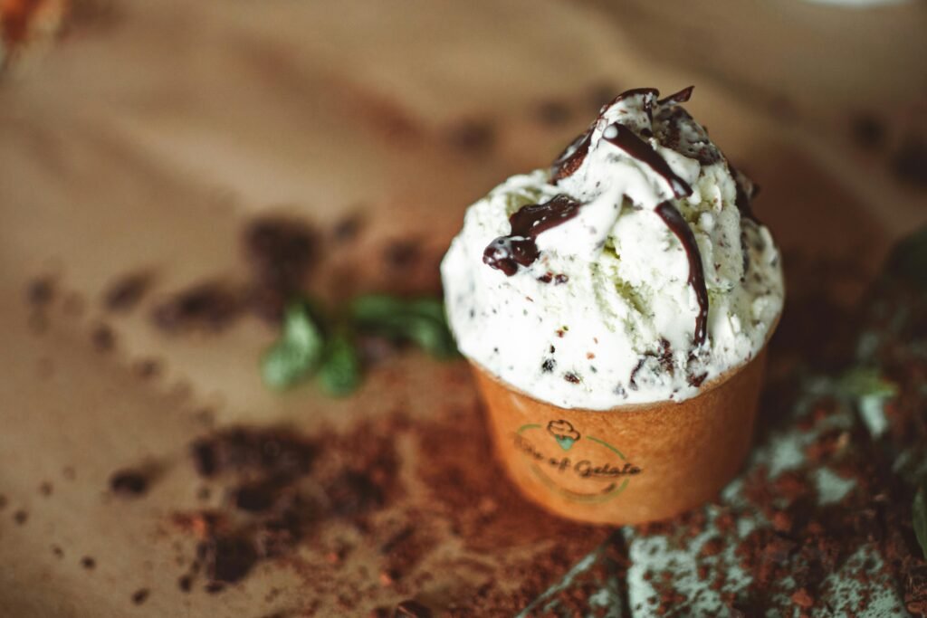 Close-up of mint chocolate chip ice cream with chocolate drizzle in a brown cup.